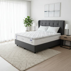 Mattress on a bed frame in a room with a rug and shelves.