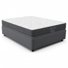 A Serenity Sleep Deluxe 100 medium comfort mattress on a dark gray upholstered box spring, shown from a front-facing perspective against a white background.